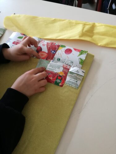 Construção da capa em cartão, forrado com papel crepe amarelo e decorada com pedaços de embalagens da Compal.
